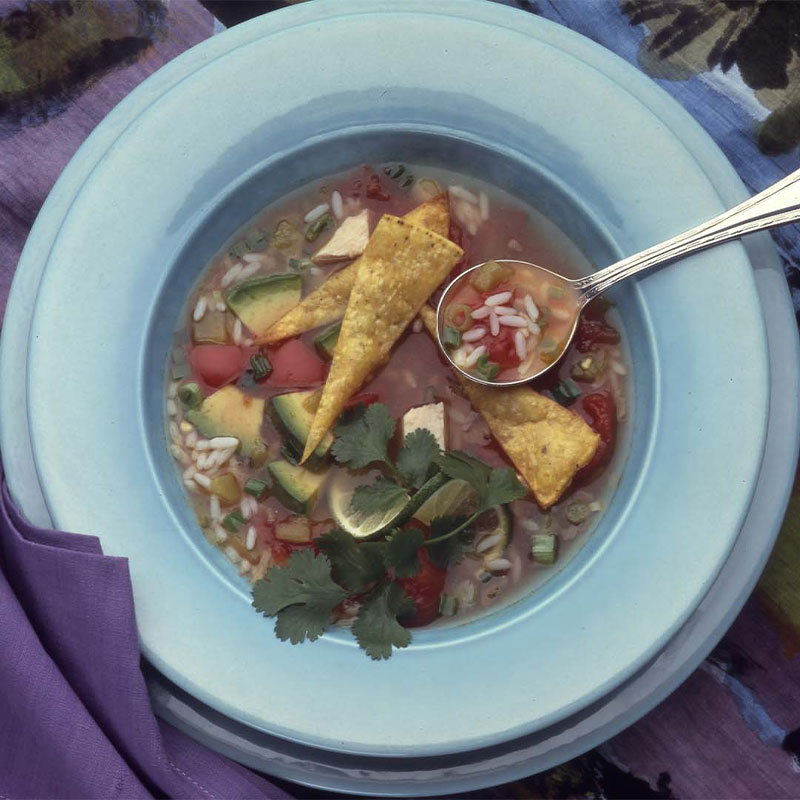 Overhead image of tortilla rice soup in a blue bowl with a spoonful resting on the bowl.