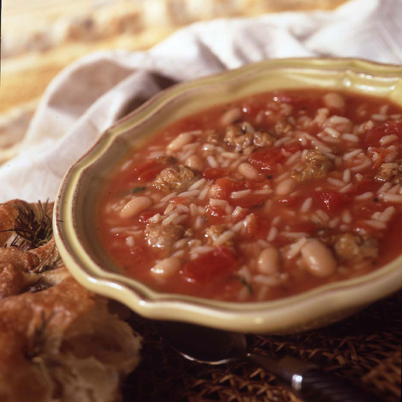 Side view of Tuscany Rice and Bean Tomato Soup in a bowl with a piece of bread to the side. 