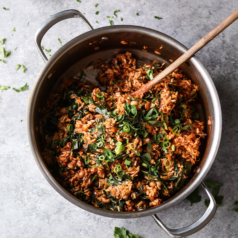 Overhead view of a large cooking pot filled with Vegan Brown Rice Jambalaya with Black Eyed Peas and Collards and topped with diced green onions.