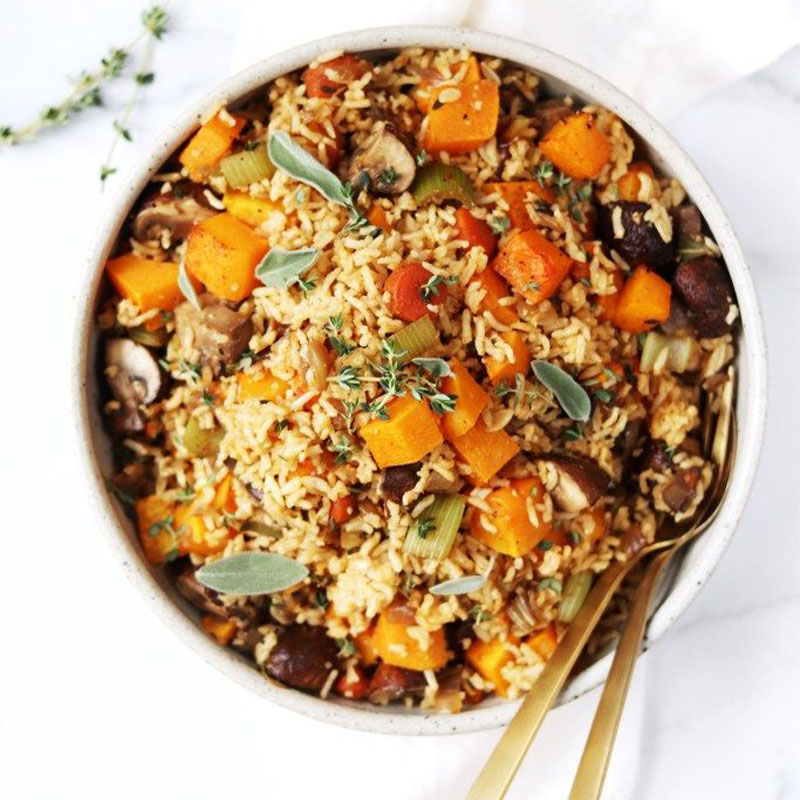 Overhead view of a bowl of brown rice stuffing with chunks of squash, mushroom, and celery exposed on top.