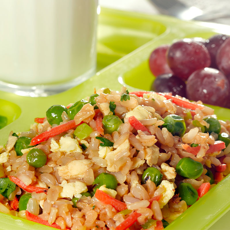 A serving of Vegetable Fried Brown Rice in a green cafeteria tray with grapes and broccoli. 