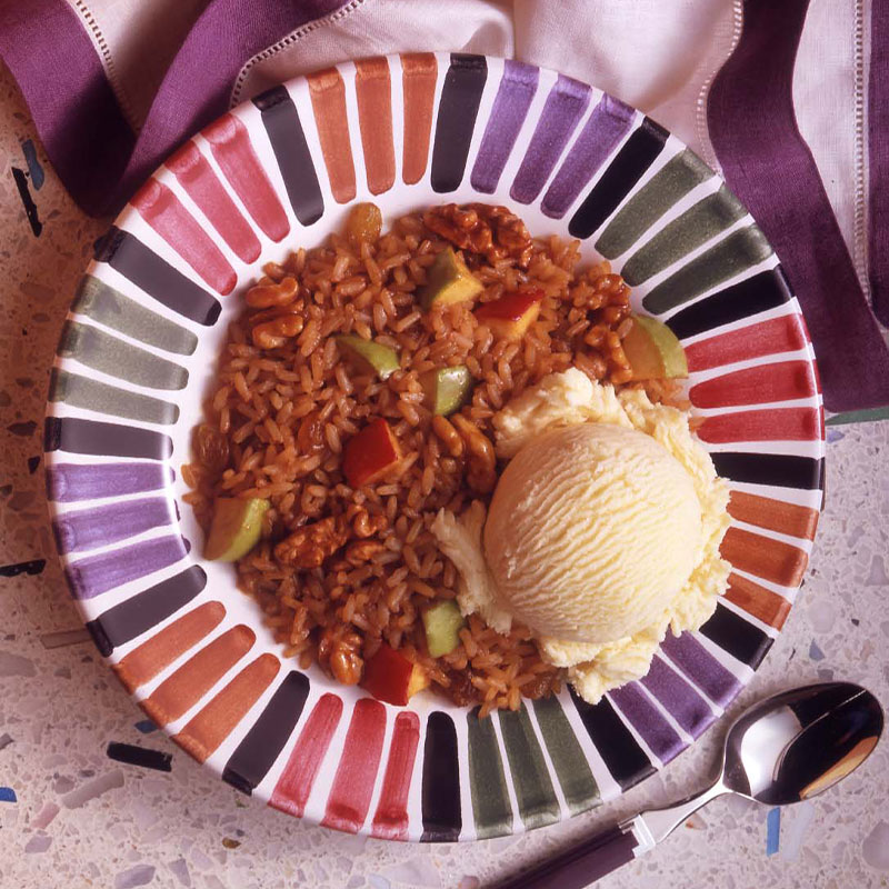 A bowl of brown colored brandied rice topped with a scoop of vanilla ice cream.