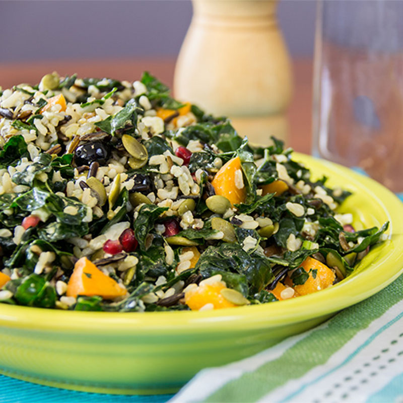 Side view of a yellow dish filled with Wild & Brown Rice, Massaged Kale Salad.