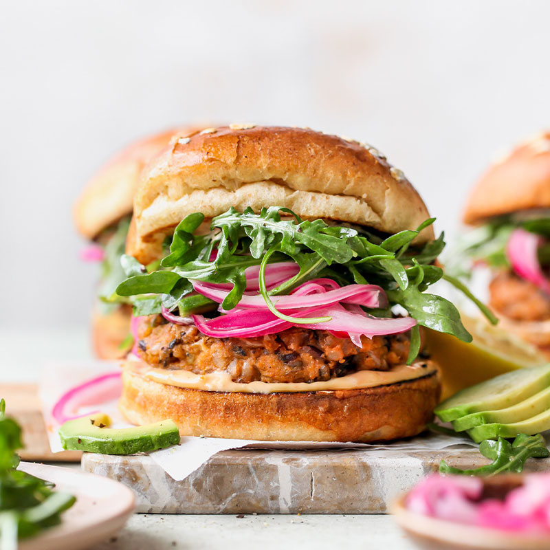 Wild Rice Burgers with Tahini Special Sauce Frontal view of one wild rice burger with additional burgers behind and out of focus.