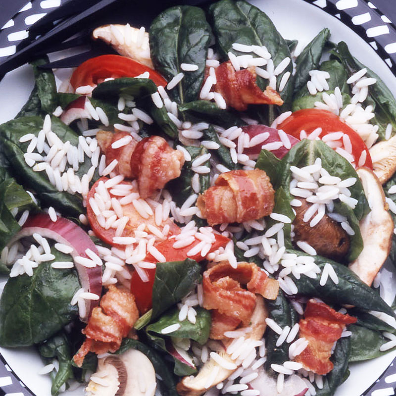 Wilted Spinach and Rice Salad Overhead shot of a spinach and rice salad with tomatoes, wrapped bacon, onion, and mushrooms on top.
