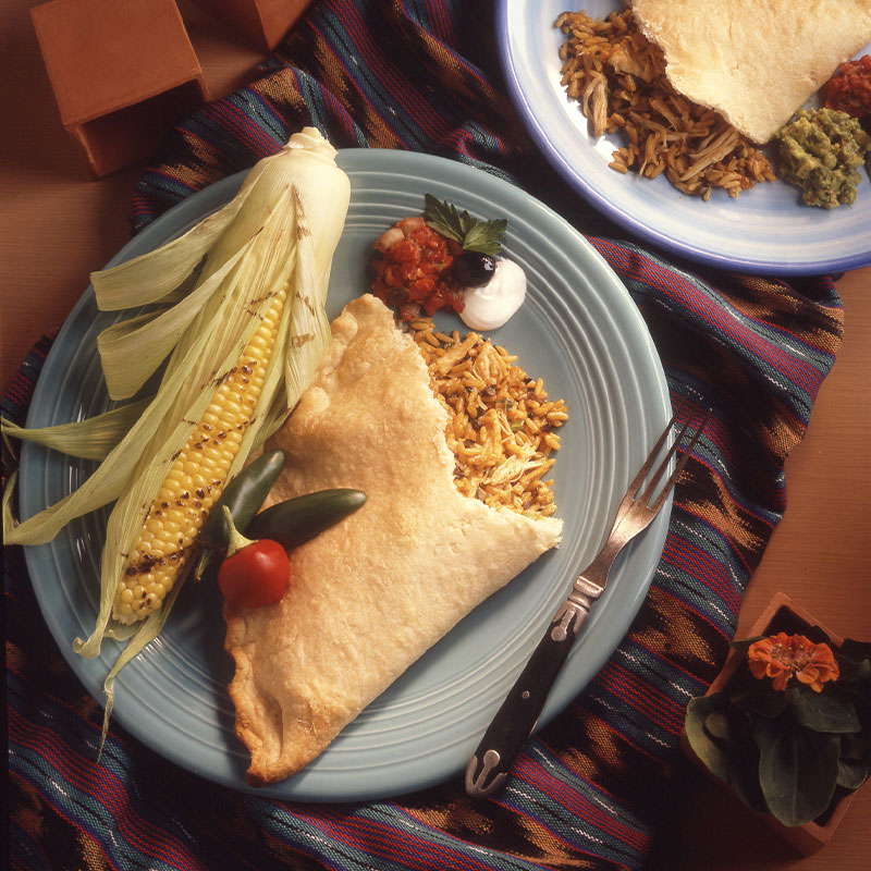 One half of a Ya Gotta Empanada with yellow rice falling out on to the plate next to a piece of corn.