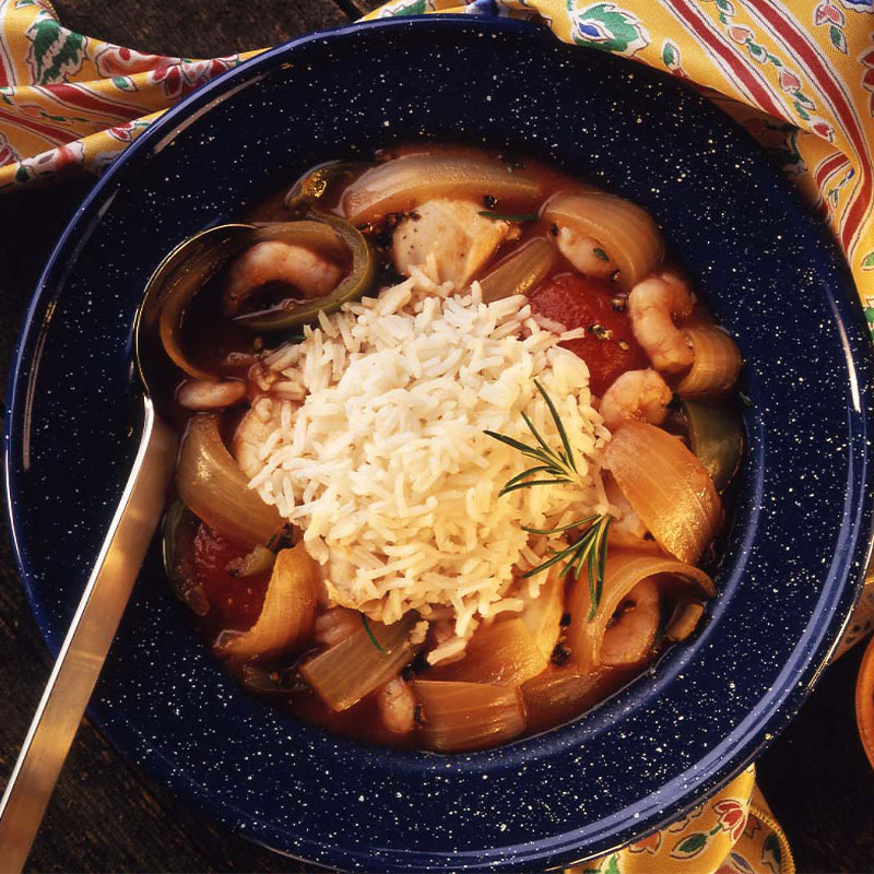 Overhead shot of a blue bowl full of Zydeco Gumbo with a scoop of white rice in the middle and a silver spoon to the side.