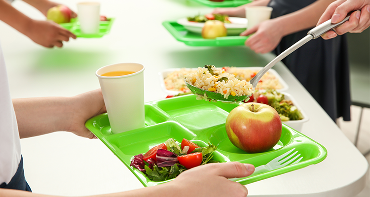 Woman placing a scoop of rice on a school lunch tray