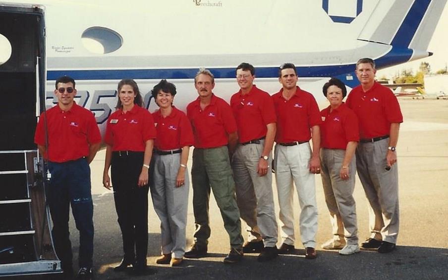 Group of people wearing red shirts stand at open door of small airplane