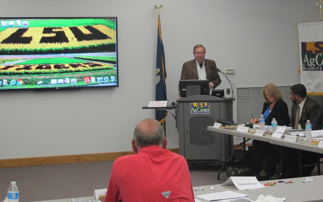 Man speaks from podium, LSU slide on screen to his right