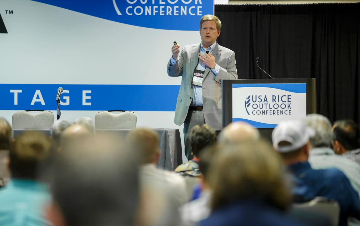 White man wearing business suit stands at podium delivering speech