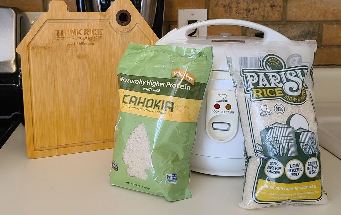 Two bags of rice propped against rice cooker and cutting board, all sitting on kitchen counter