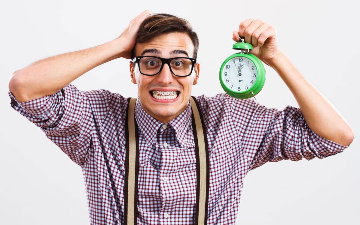 Boy with braces wearing suspenders and dark-rimmed glasses holds alarm clock
