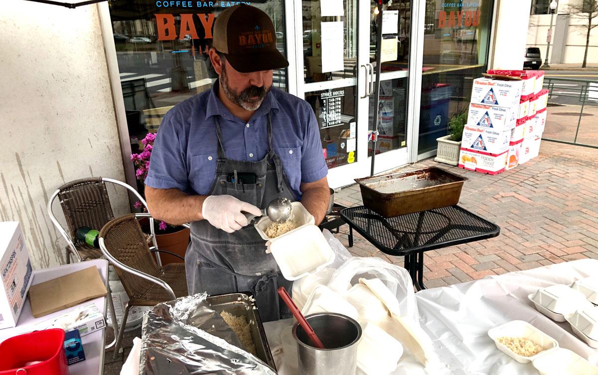 Man wearing apron and ballcap serves rice at catering table on sidewalk outside Bayou Bakery