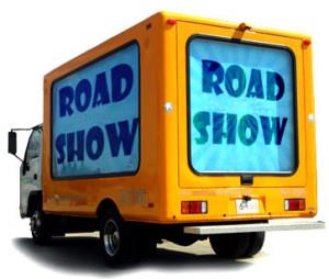 Moving truck with white cab and yellow body with text "Road Show" on blue background