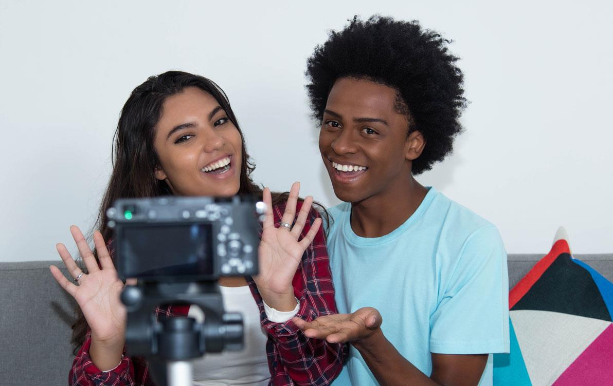 Two students sit on couch in front of camera-on-tripod