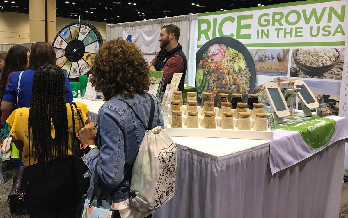 2022-FNCE,-C.-Jacobs at USAR booth with GITUSA poster and glass jars filled w/rice on table