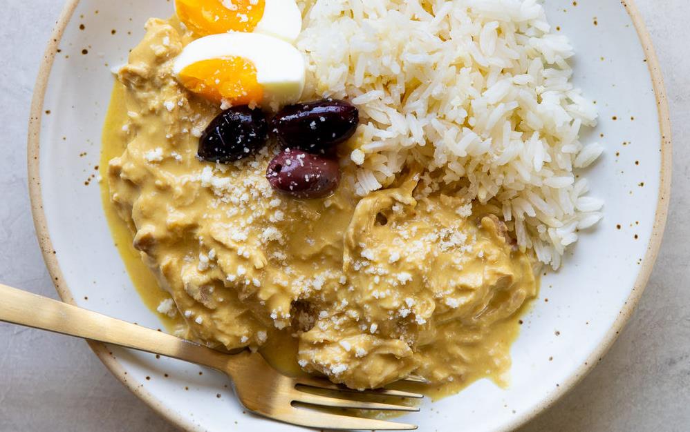 Aji de Gallina, Peruvian chicken stew with hard-boiled eggs and olives on white plate w/gold fork