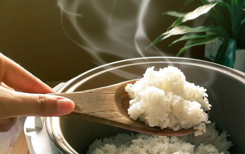Hand-holding-wooden-spoonful-of-cooked-rice-from-rice-cooker