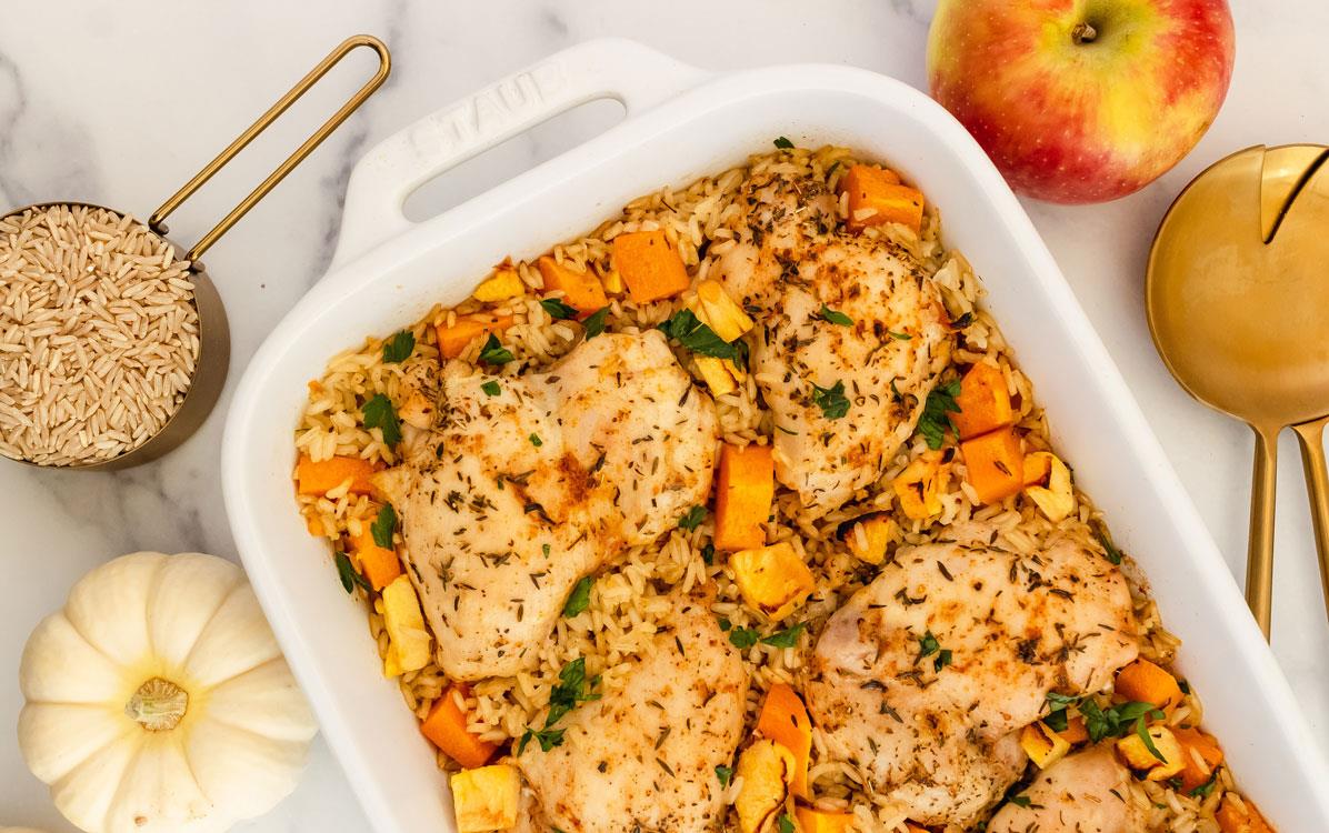 Fall-Chicken-&-Rice-Bake, surrounded by apple, white pumpkin, & cup of brown rice