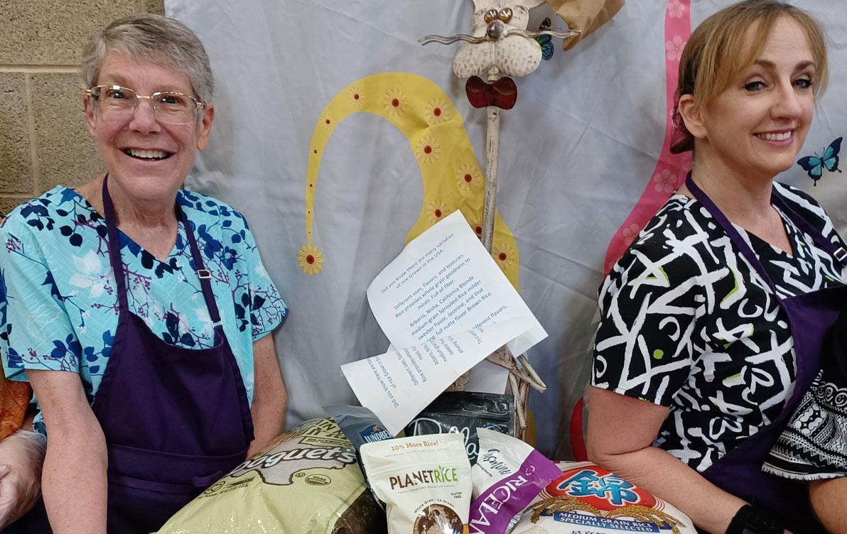 Two school lunch workers stand next to table filled with US rice samples