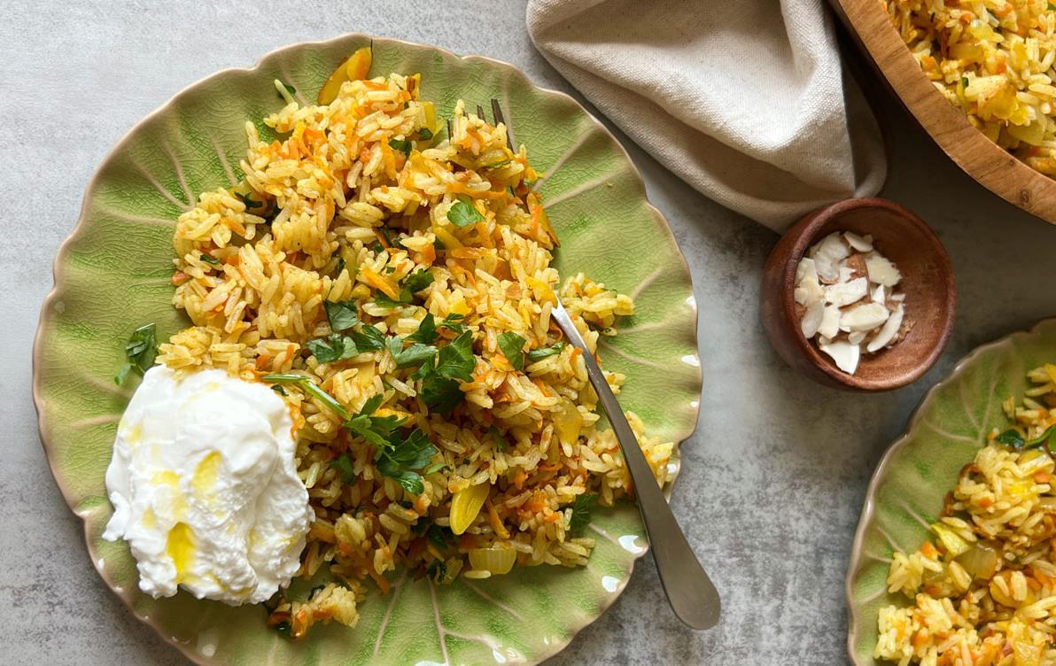 Orange-Zested-Rice served on green dish surrounded by a bowl of slivered almonds and a beige napkin