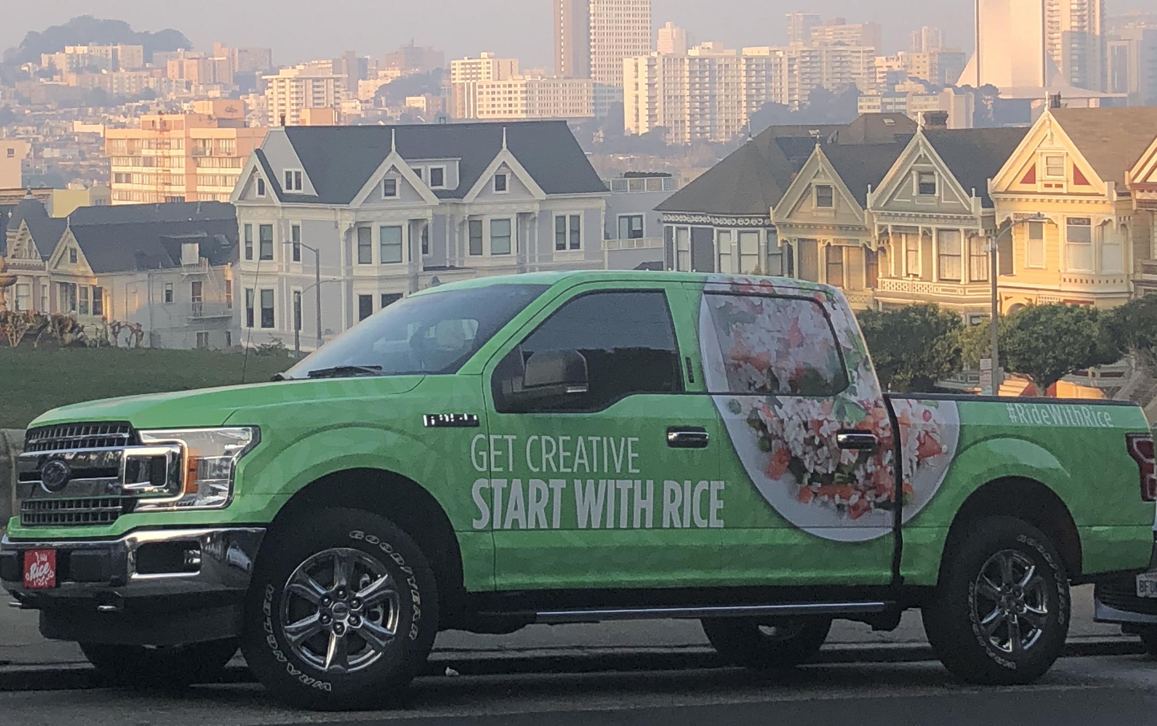 Green Rice Truck covered with images of rice and text "Get Creative, Start with Rice," parked on street in front of Painted Ladies, colorful row houses in San Francisco