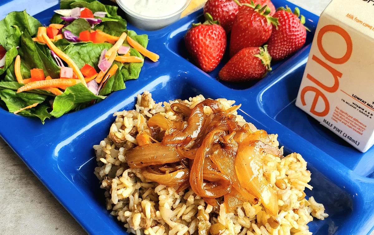 School lunch of rice with onions, strawberries, and milk on blue tray
