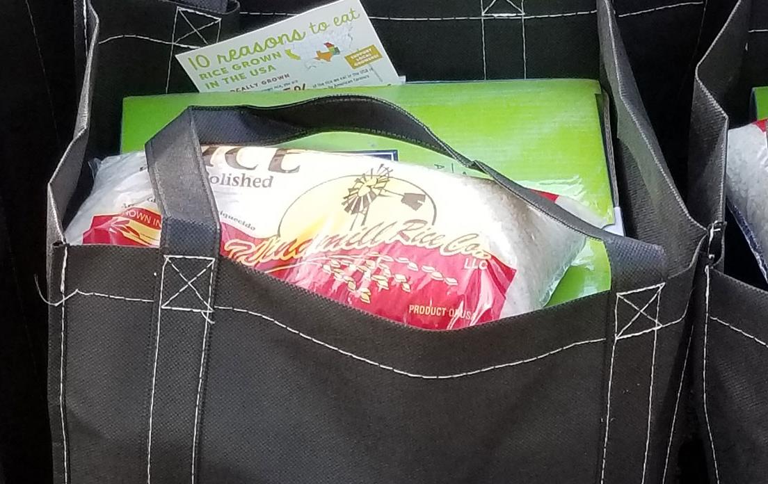 Black shopping bag filled with green box and bag of rice, text on side says "Get Creative, Start with Rice"