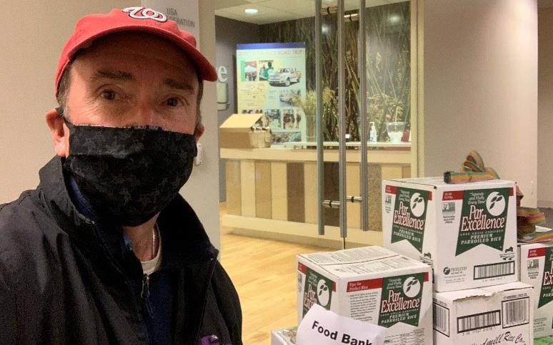 White man wearing Nationals ballcap and black face mask stands next to rice boxes for food bank donation