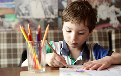 Young boy sits at table coloring with colored pencils in a glass