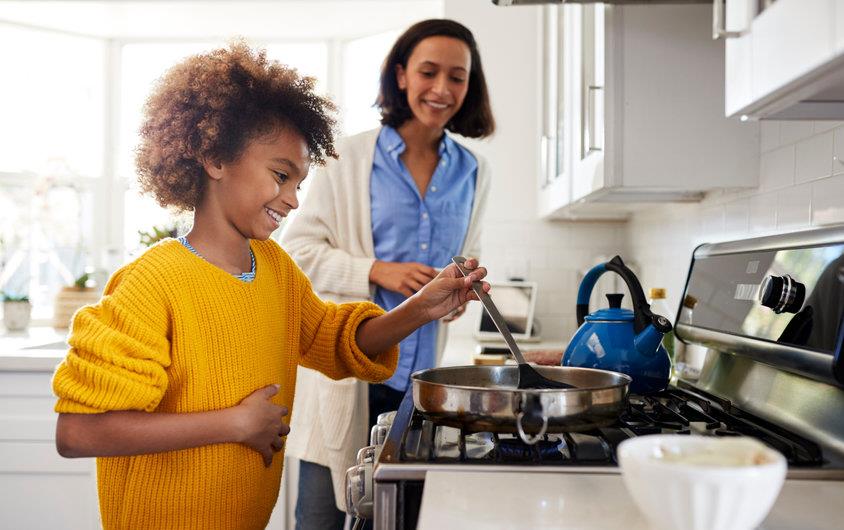 Young girl cooking on stove while mother looks on