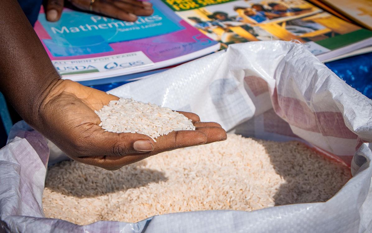 Hand-holding-fortified-rice-from large bag with other hand on top of pile of school-books