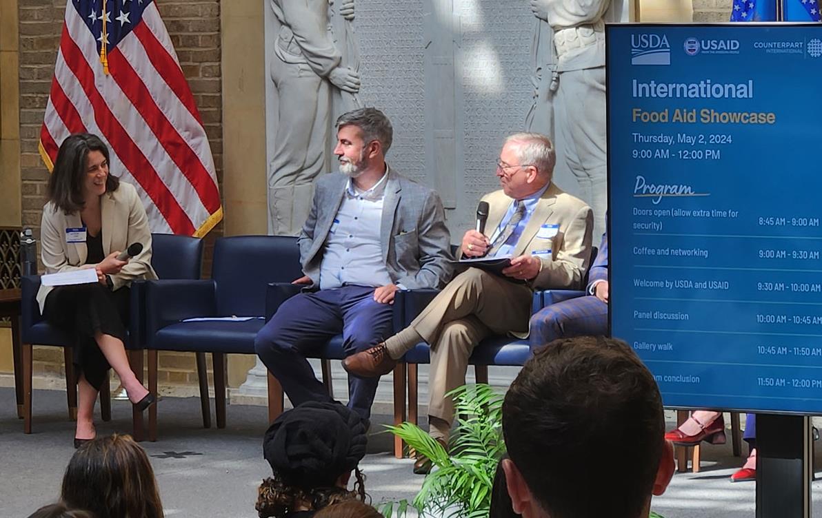 Intl-Food-Aid-Showcase,-panel seated on stage, American flag and statues in background