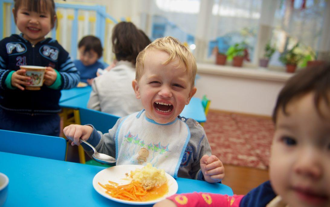 Smiling white child wearing bib, holding spoon with plate of rice