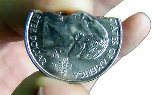 Close up of fingers holding silver coin bitten in two 