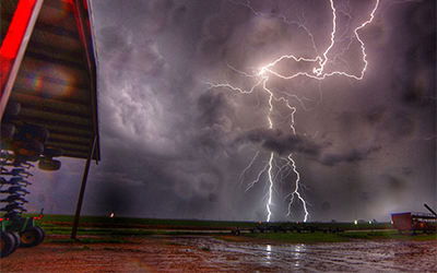 Dark-sky-with-lightning hitting ground, farm equipment in foreground, Zach-Worrell-photo