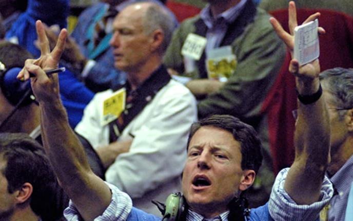 Crowd of traders on stock market floor, man in foreground has both arms raised and is shouting