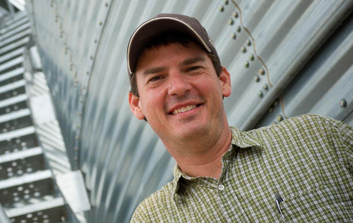 Jeff-Rutledge wearing ballcap standing in front of grain bin