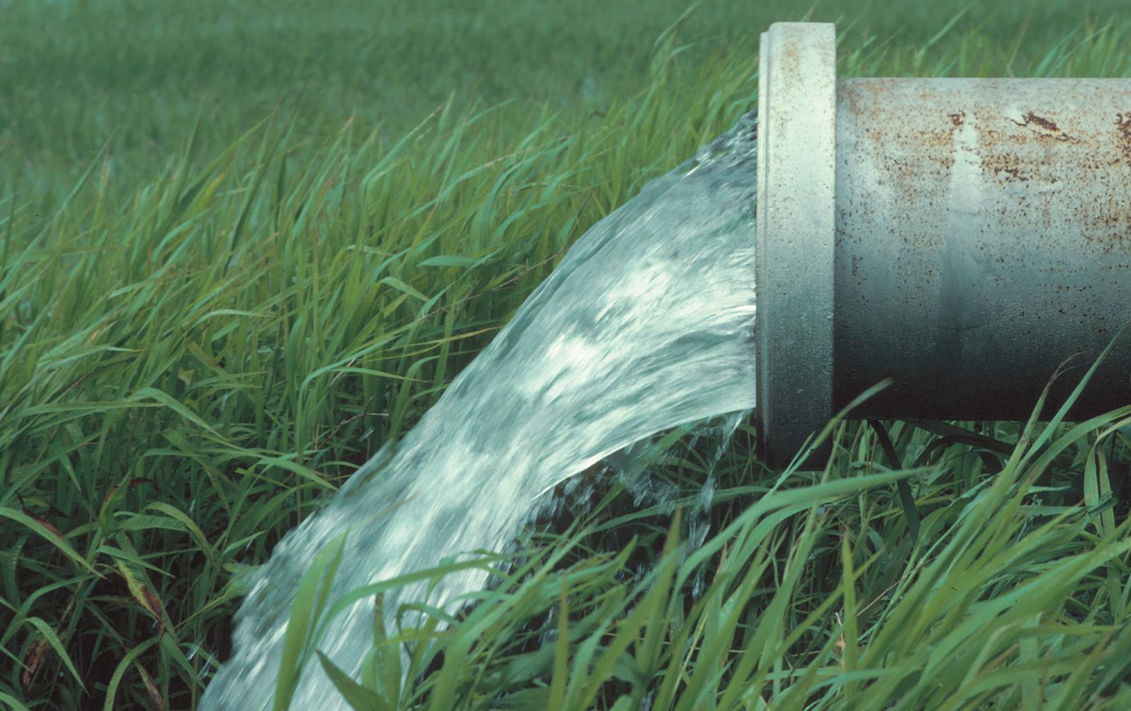 Water pouring out of large metal pipe, flooding AR rice field