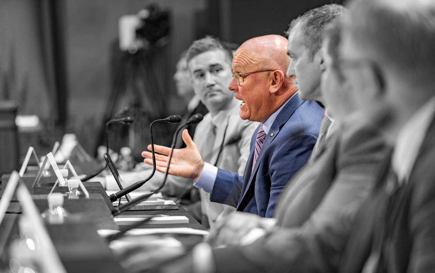 B/W photo of group of men testify before Congressional Committee, Rich Hillman highlighted in color