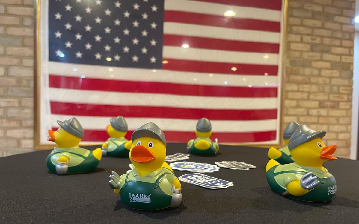 USAR rubber ducks on table w/US-grown rice decals, large American flag in background