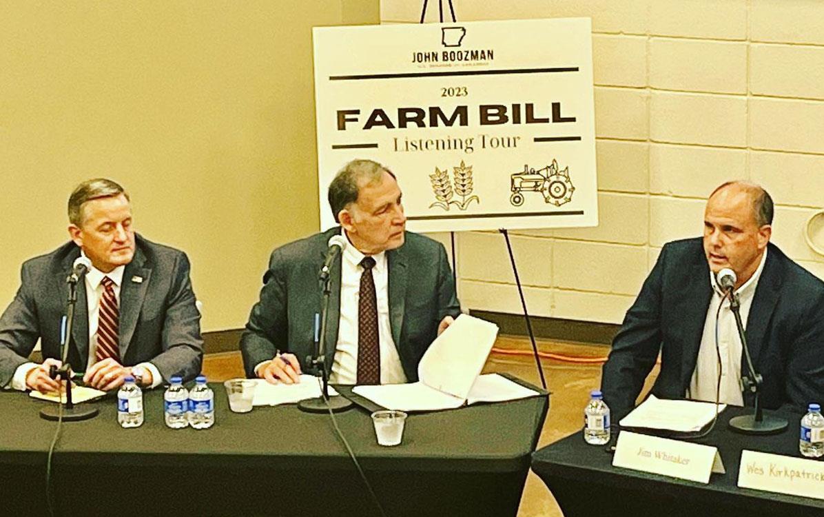 Three men sit at table in front on microphones, Farm Bill poster on easel in background