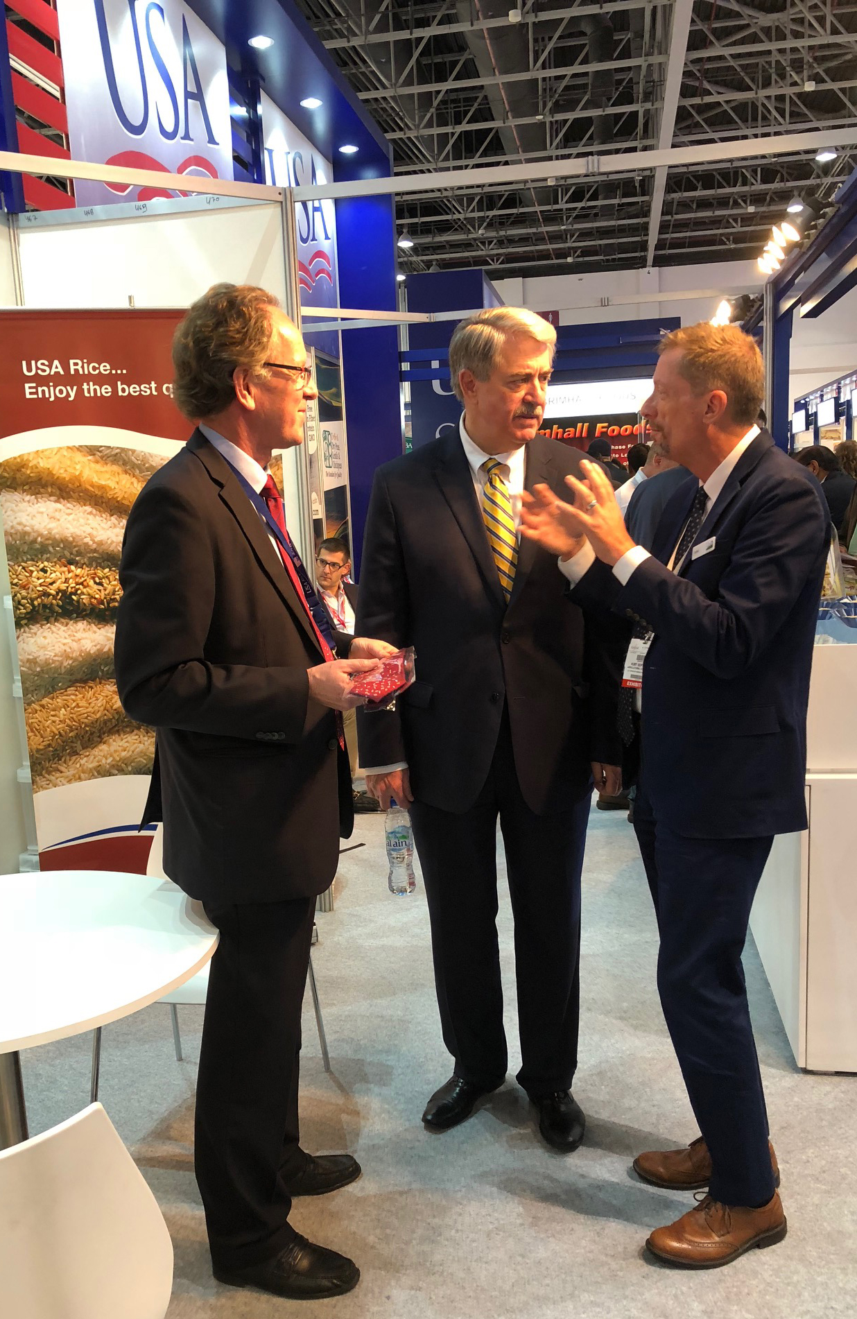 Undersecretary McKinney at USA Rice booth at Gulfood Show 2018 [image description: three men standing together talking in exhibit hall]