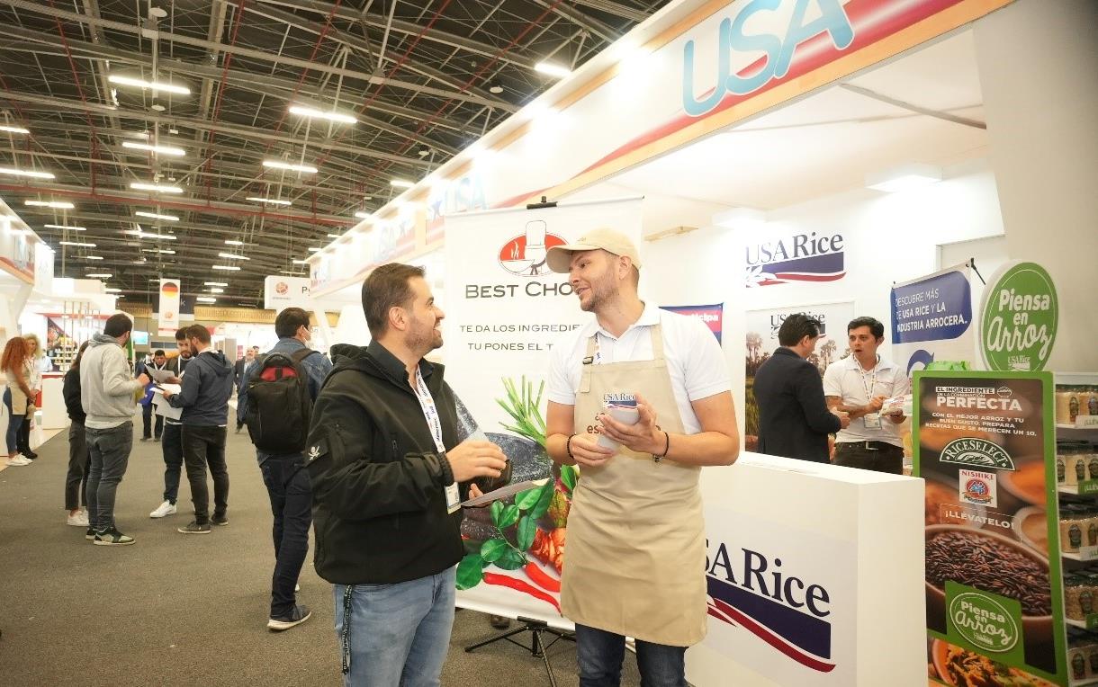 USA Rice booth with logos and staff wearing USAR aprons, talking with attendees
