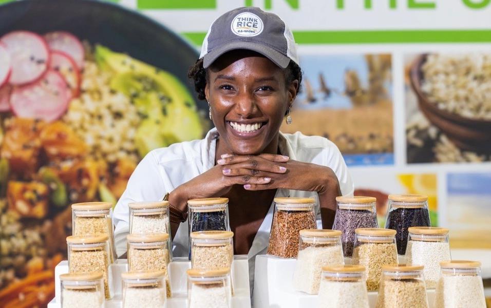 2022 SIAL, black woman wearing Think Rice ballcap stands behind rice displayed in glass jars
