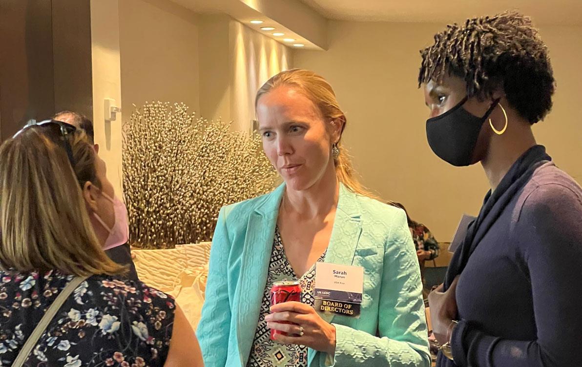 Three women, two wearing face masks, stand staring at one another 