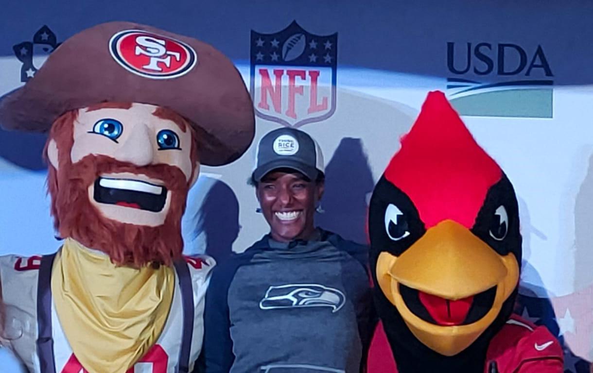 Black woman wearing Seattle Seahawks sweatshirts stands between 49ers & AZ Cardinals mascots