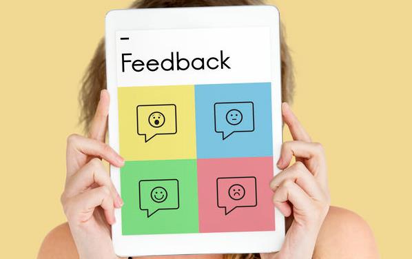 White woman holds iPad in front of her face with 4 color blocks showing different emojis