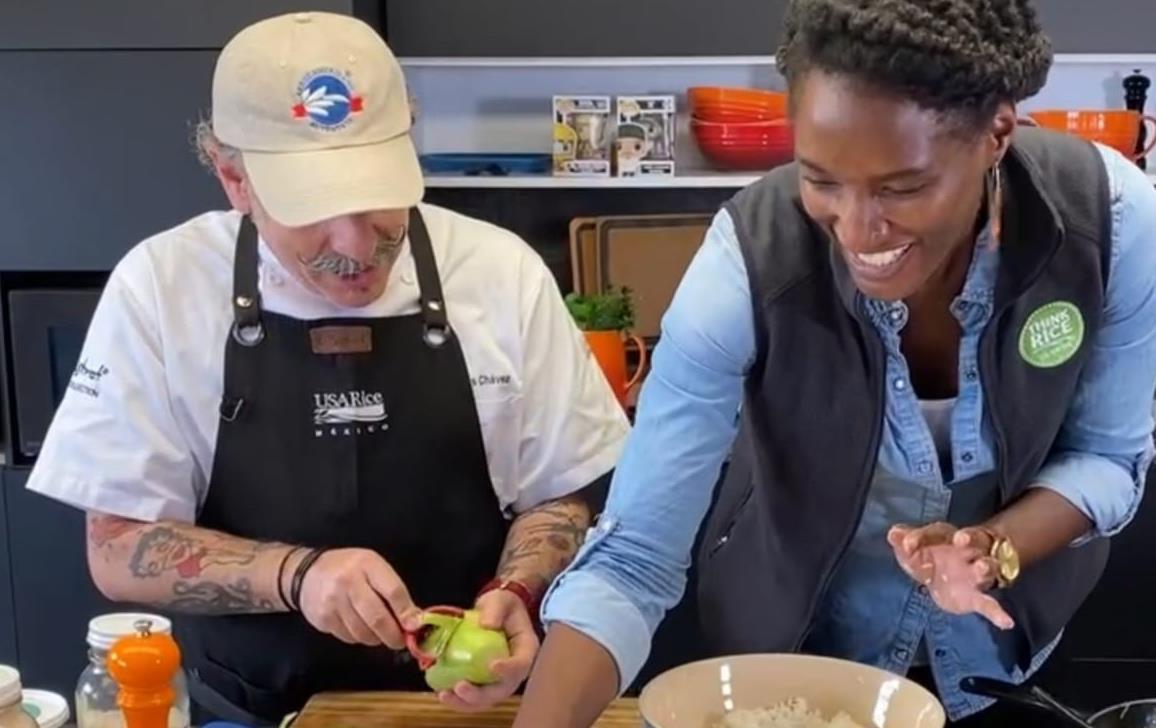 A man and woman wearing USA Rice logo items (hats, vests, aprons) cook together